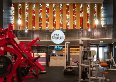 Blick auf das leuchtende Logo und Buntglas-Fenster von The Church Sports & More Rheine über dem Gerätebereich.