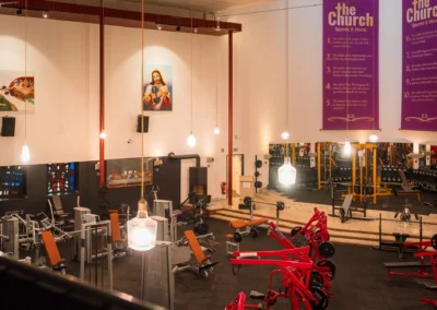 Blick auf die Trainingsfläche im Kirchenschiff von The Church Sports & More Rheine mit roten Hammer Strength Kraftgeräten und Motivationsbannern.