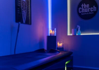 Überwassermassage-Liege im blau beleuchteten Wellnessbereich von The Church Sports & More Rheine mit stimmungsvollem Kerzenlicht.